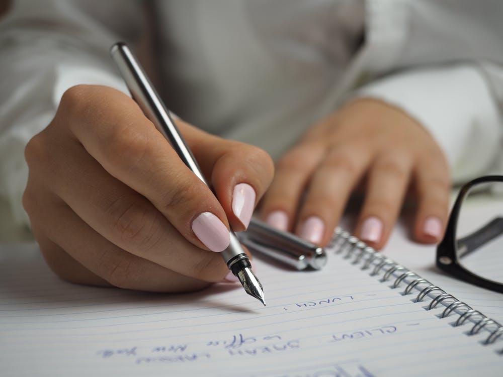 kvinde med gellack negle skriver i notesbog